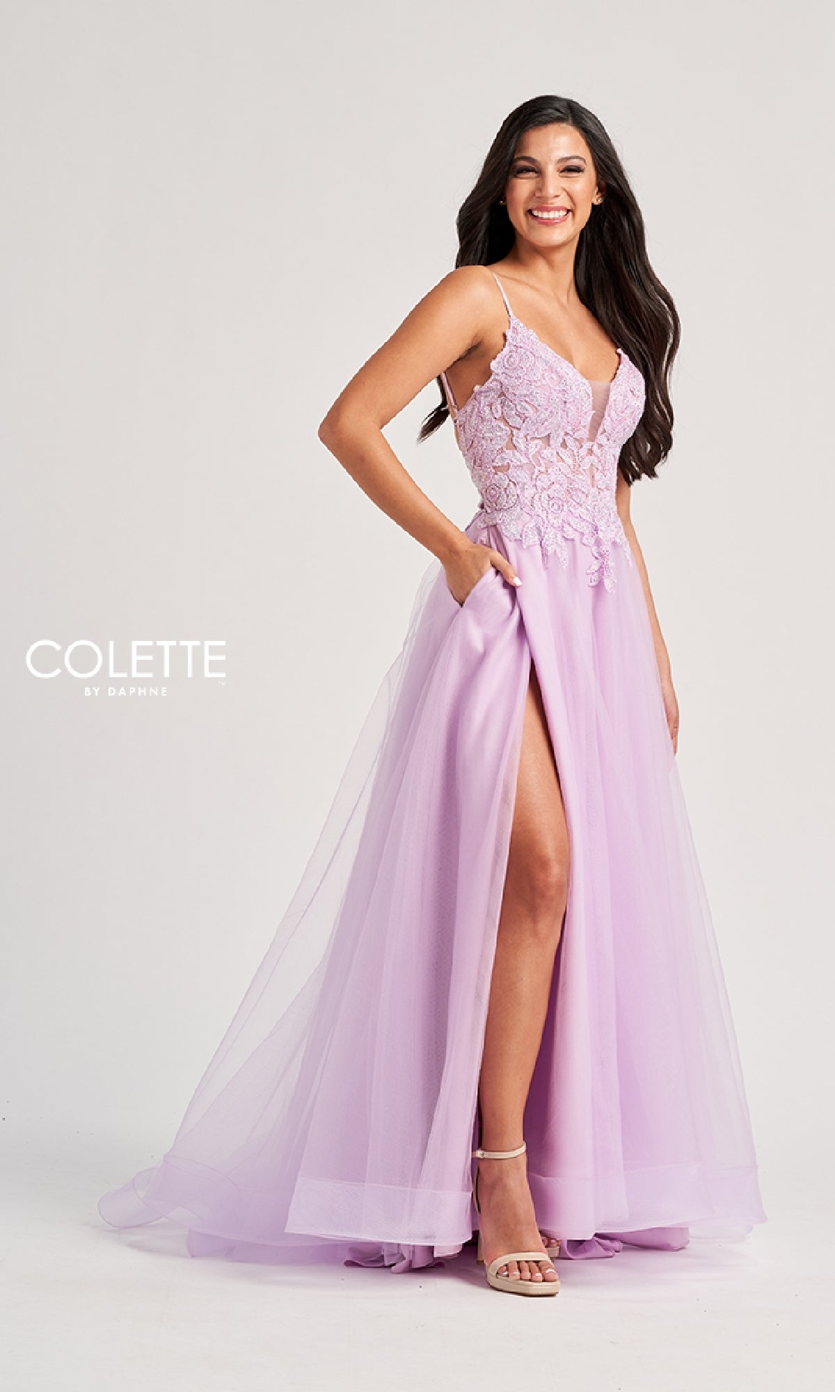 A woman smiles with one hand in her pocket, wearing the Colette CL8100 long prom dress featuring a pastel tulle skirt, lace embroidery bodice, spaghetti straps, and a high slit.